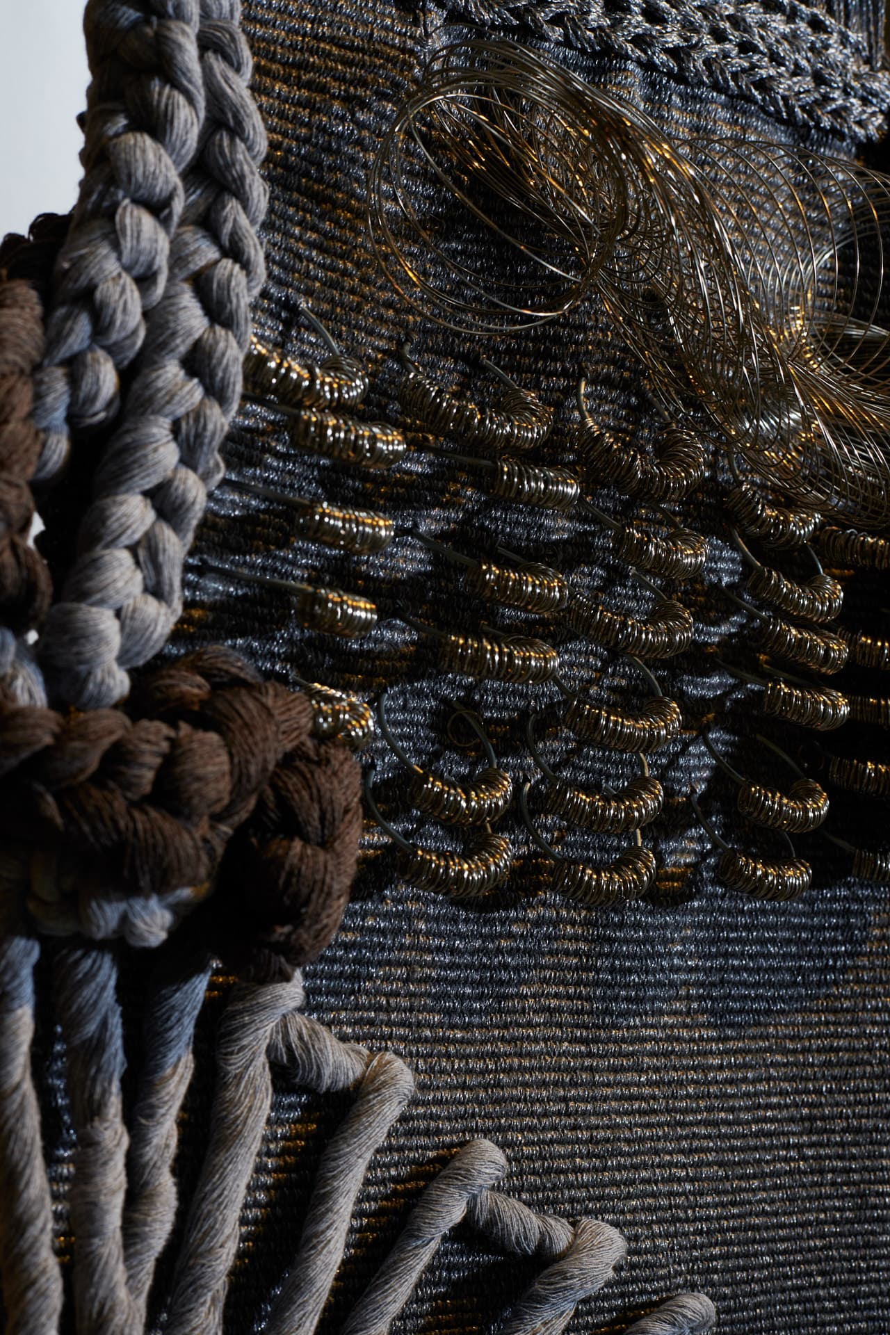 Close-up of the artwork ‘Gestando en la fria sombra’, composed of grey braided threads and textured elements made of metal wire.