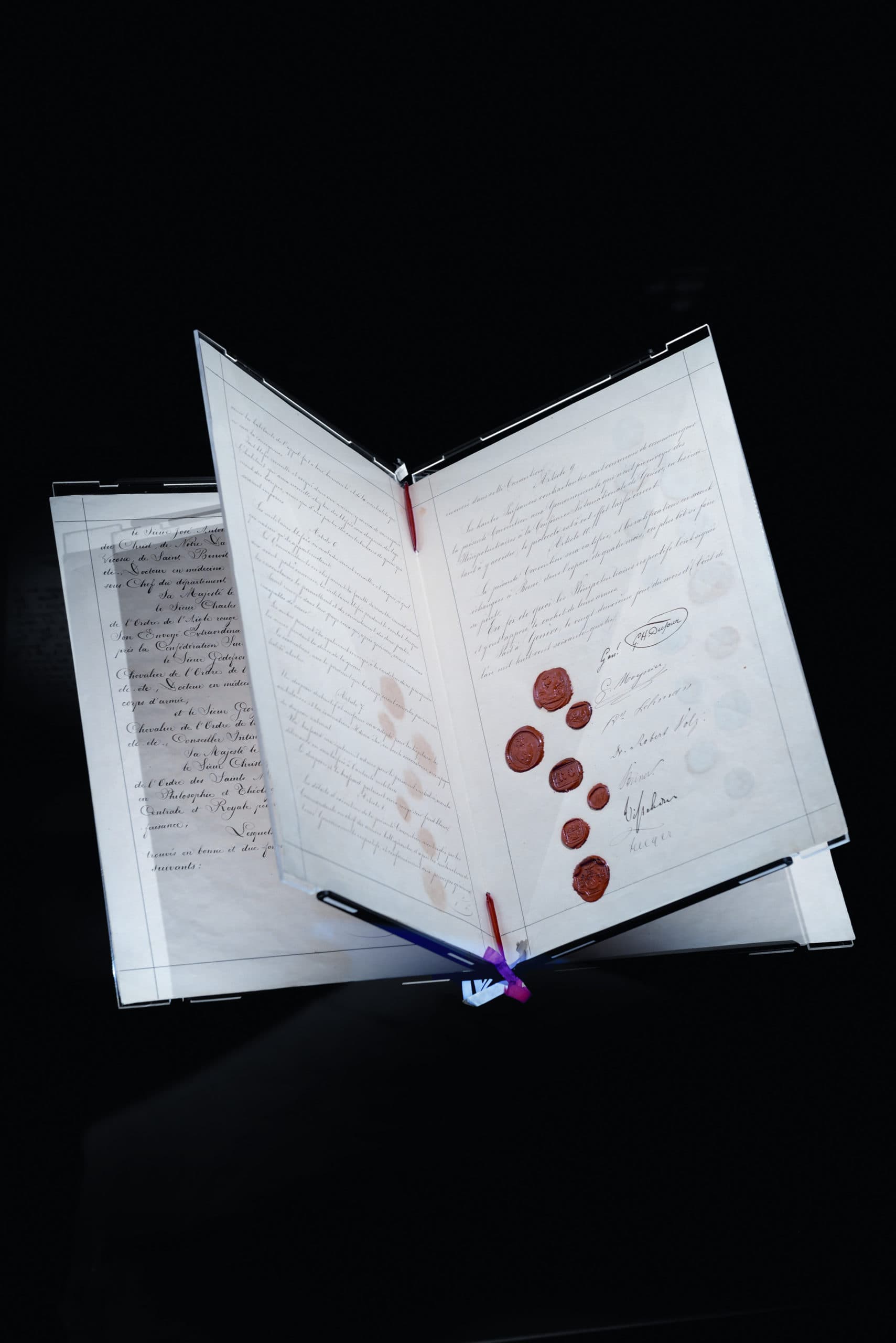Ancient handwritten documents fanned out, featuring cursive script and red wax seals, displayed against a black background.