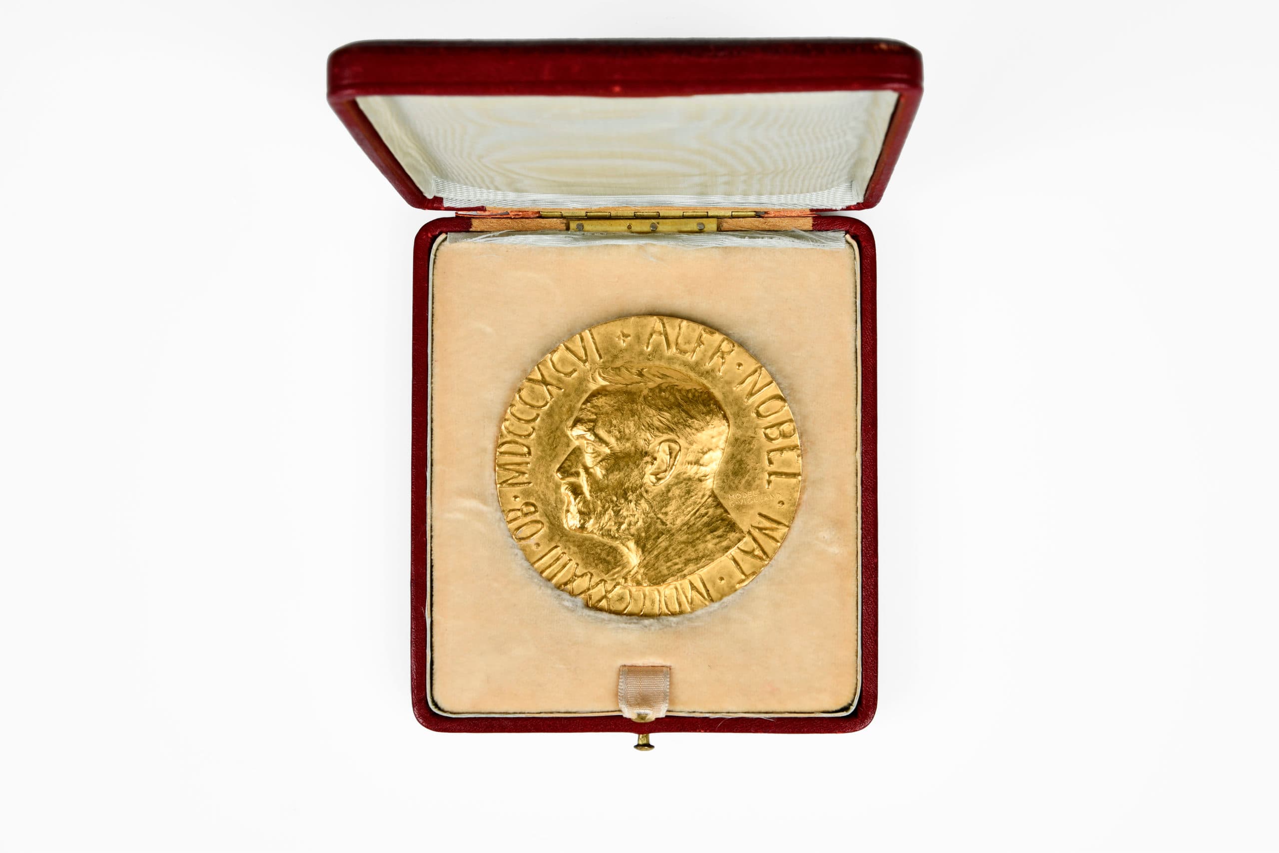Médaille dorée représentant un profil d'homme, présentée dans un écrin ouvert rouge et doublé de tissu clair.