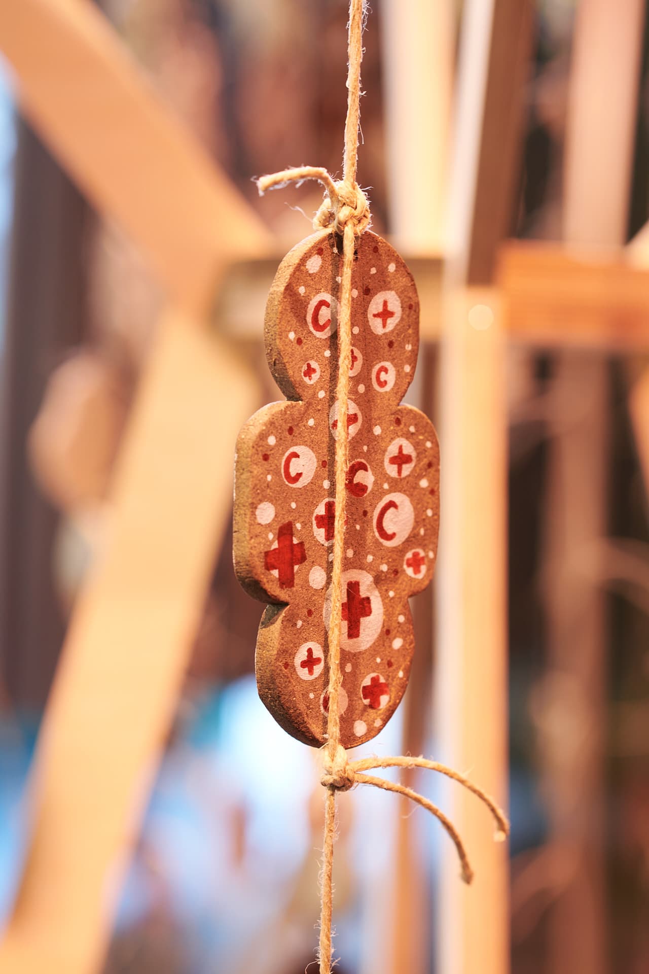Gros plan sur un objet décoratif en céramique suspendu, composé de motifs de croix et demi-lunes rouges dans une lumière chaude, détaché d'un fond flou.
