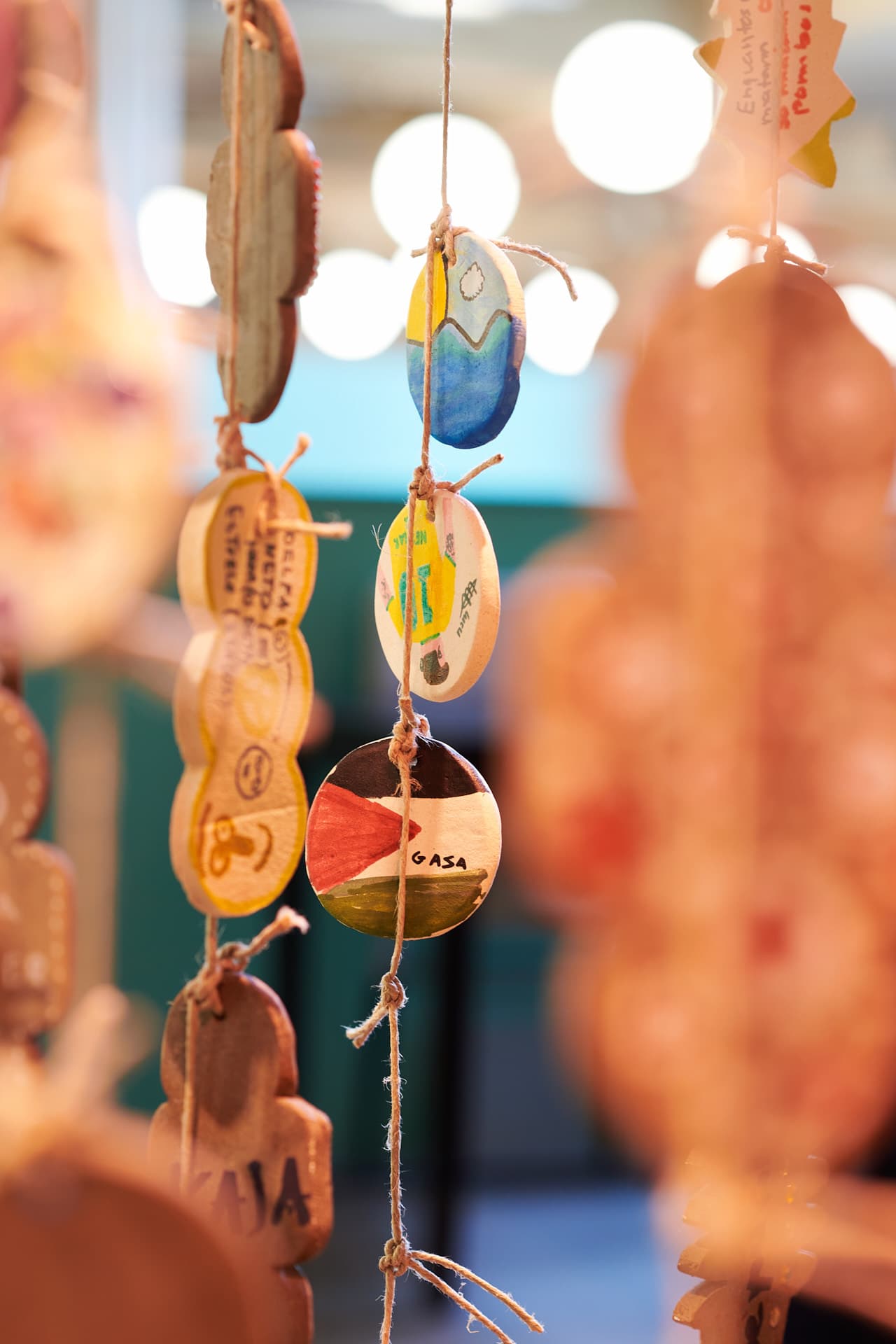 Close-up of circular ceramic decorative objects hanging from above, decorated with designs and text in warm light, set against a blurred foreground. In the centre of the image, one of the objects depicts the Palestinian flag with the inscription ‘Gaza’.