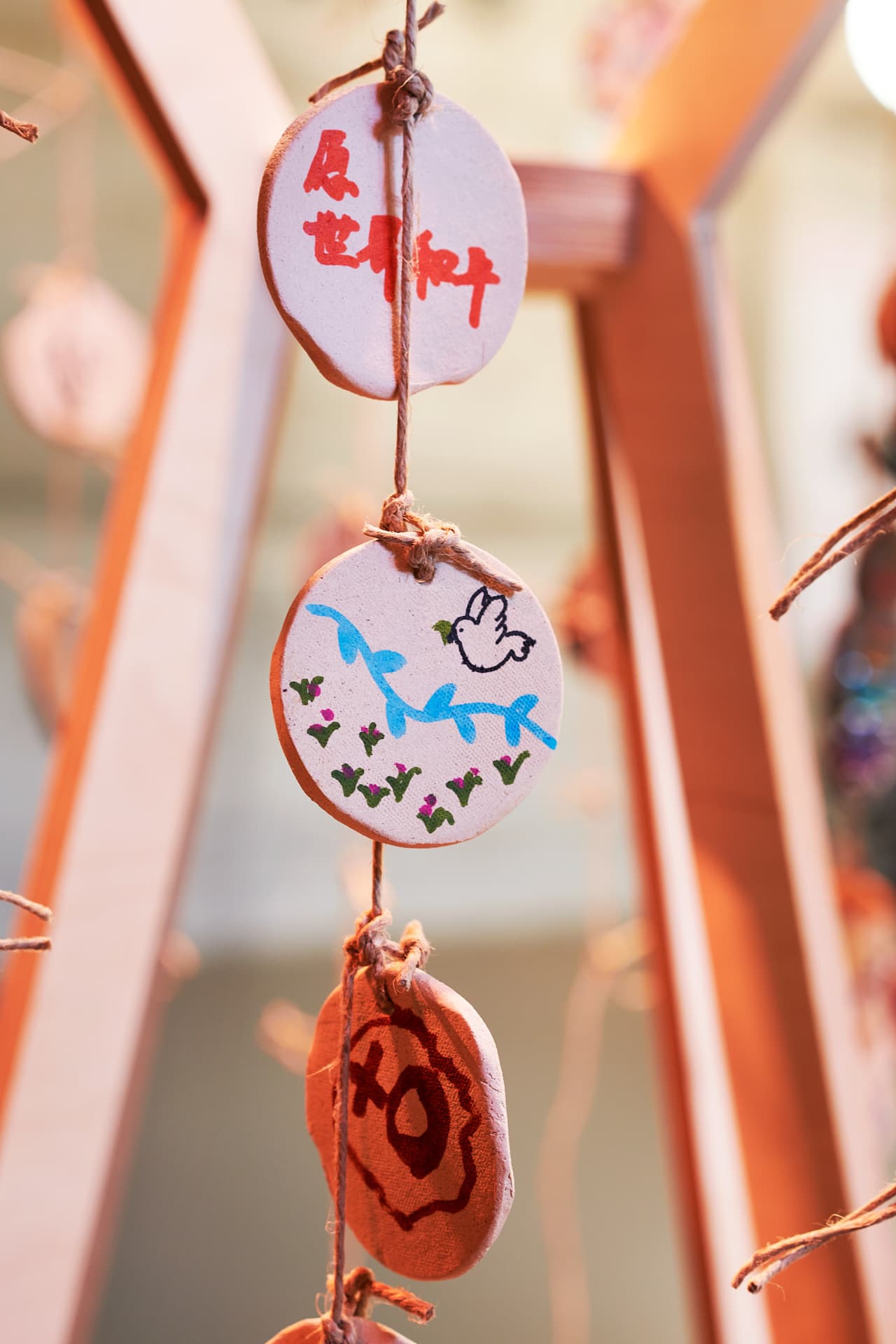 Close-up of circular ceramic objects suspended by a string from a wooden structure, decorated with colourful inscriptions and a dove.