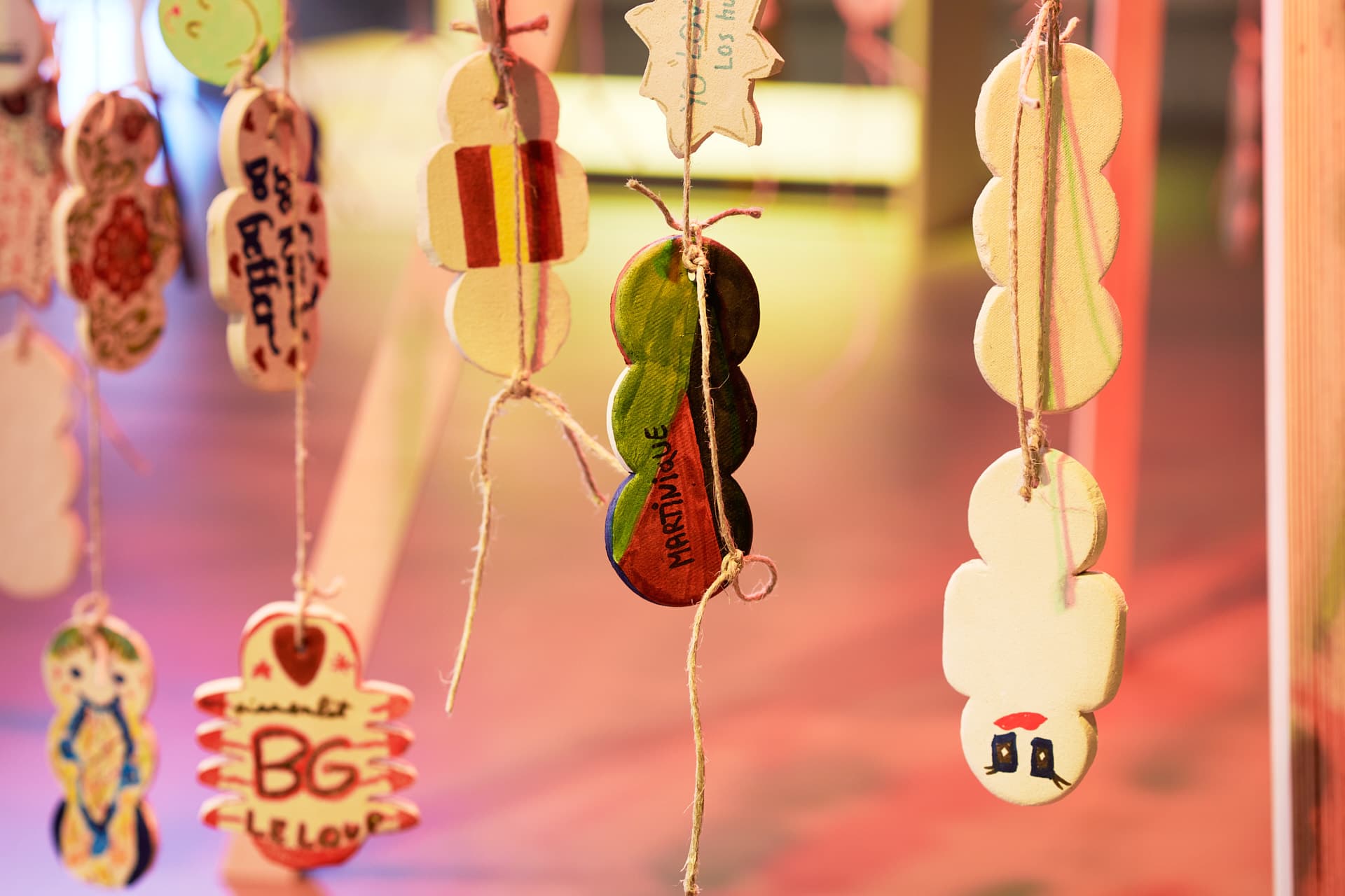 Hanging circular ceramic decorative objects, decorated with designs and text, bathed in warm light, set against a blurred foreground.