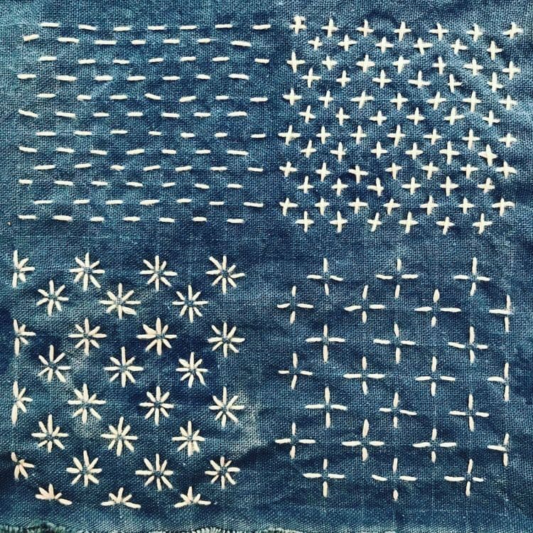 Sashiko embroidery stitches in the shape of crosses, stars or lines, made with white thread on indigo-dyed fabric.