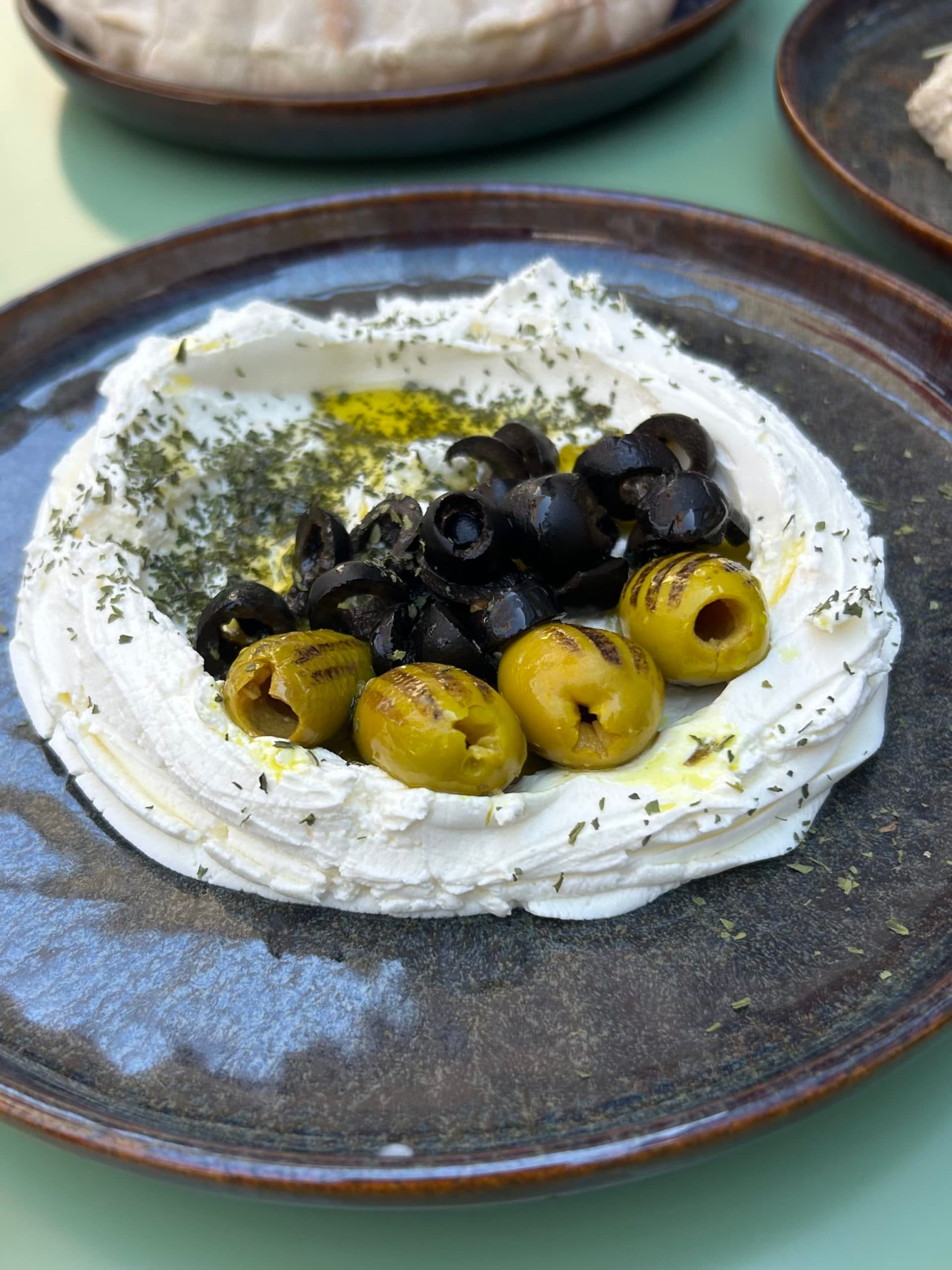 A plate of fresh cheese garnished with black and green olives, with aromatic herbs.